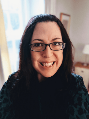 Author Kate Frost. Image of a smiling woman with long dark hair wearing glasses and a black sweater.